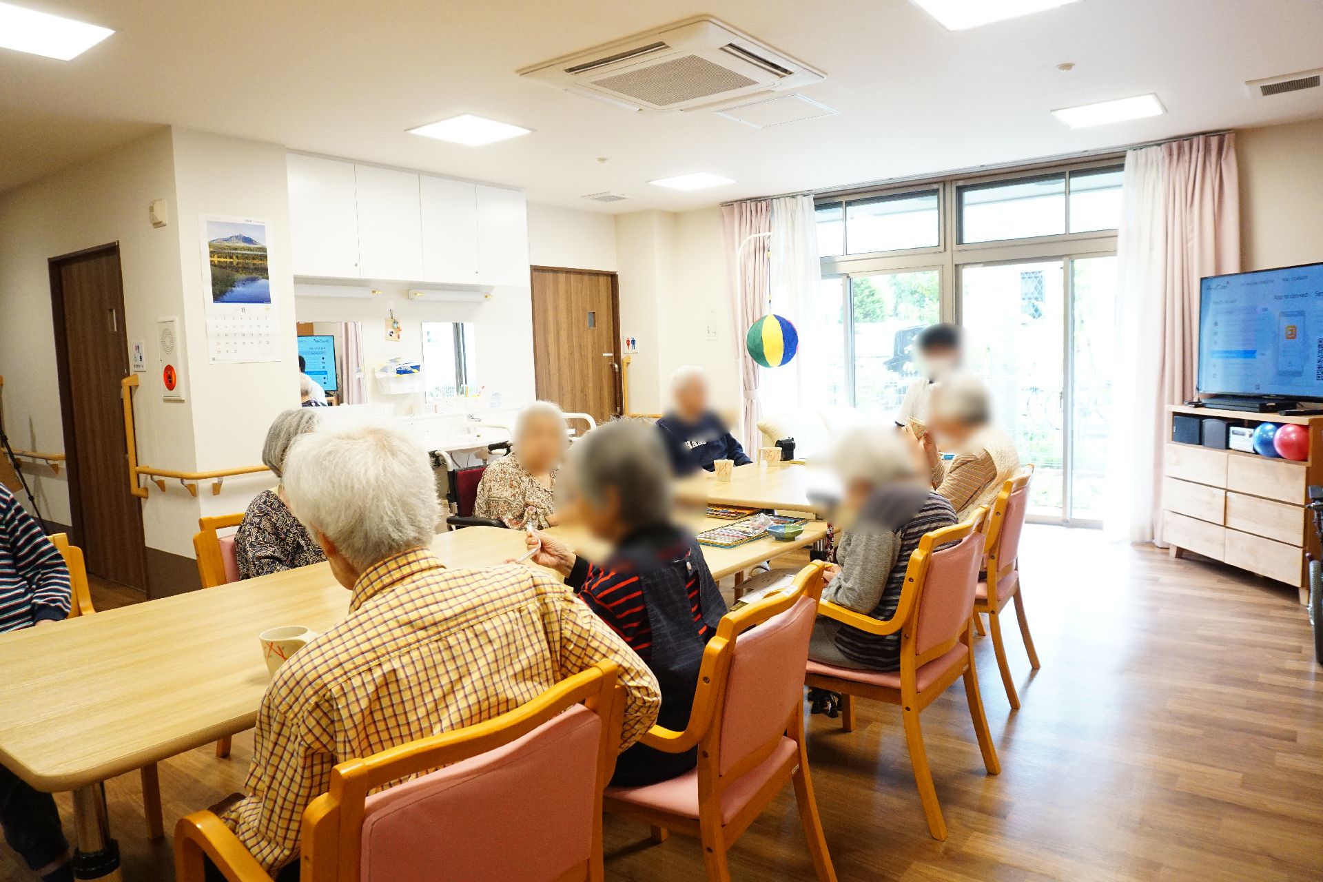 テレビが設置され、テーブルの周りに入居者が集まっているリビング
