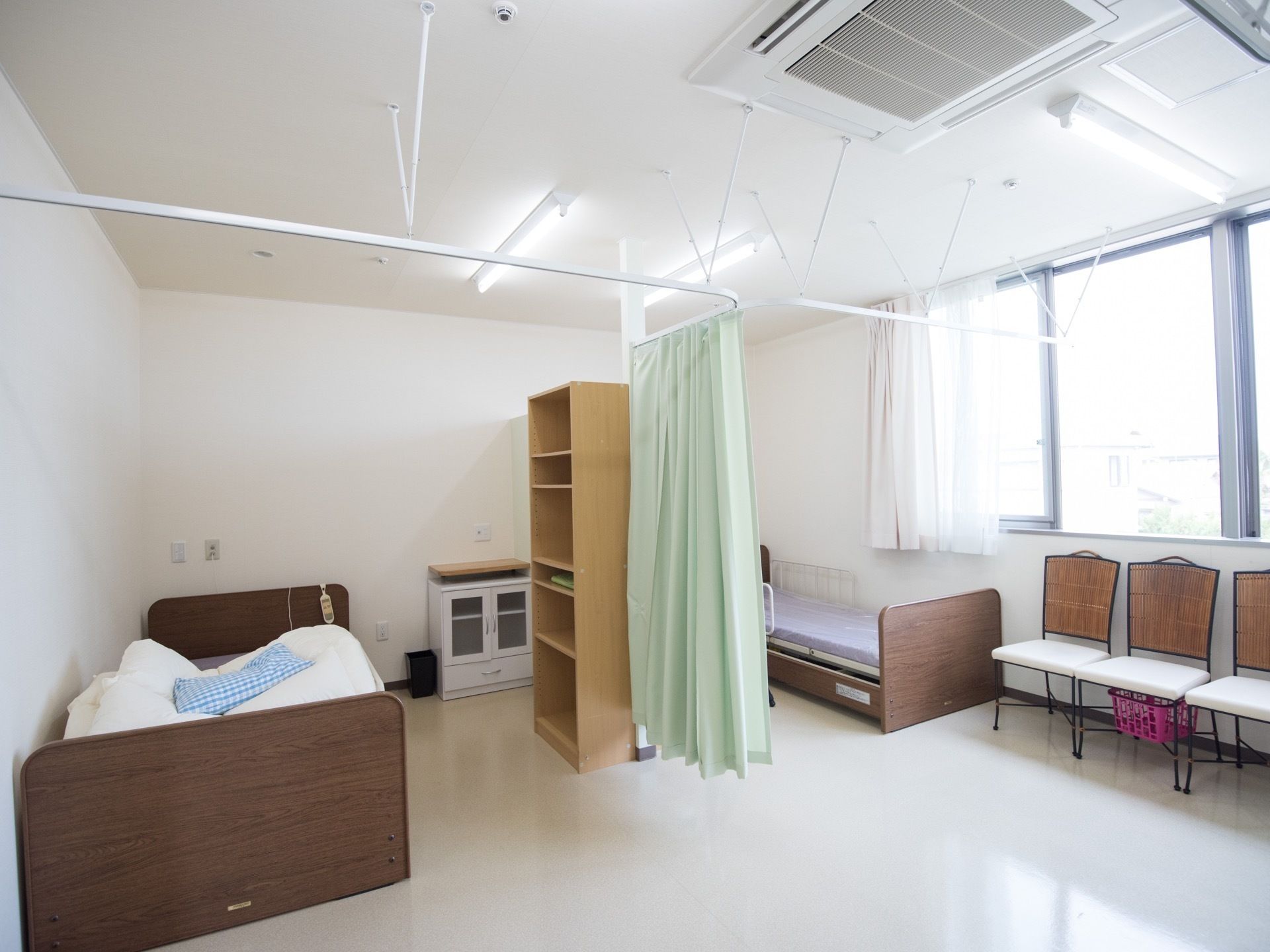 窓が設置されたお二人用の居室である。両サイドの壁際に介護用ベッドが設置され、仕切り用のカーテンが中央に掛けられている。