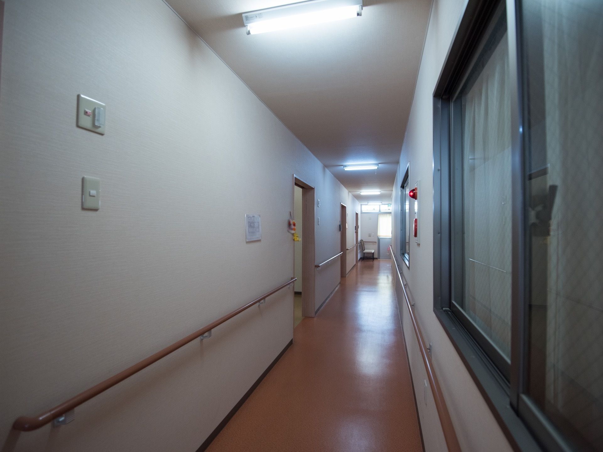 居室前の廊下はすっきりと見通しが良い。壁には窓や非常ベルが設置され、両サイドに手すりが取りつけられている。