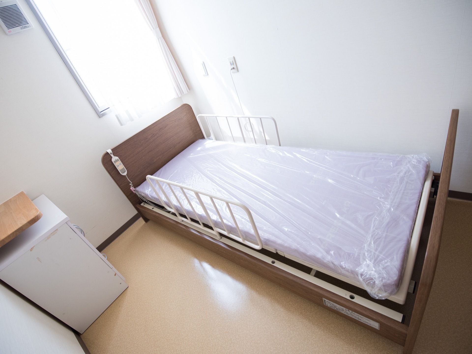 ご使用前の介護用ベッドが置かれている。ラベンダー色のマットにビニール袋が掛けられ、転倒防止フレームが両サイドに設置されている。