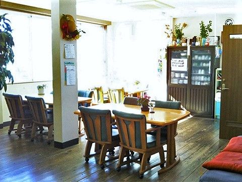 木製のダイニングテーブルが複数置かれ、ぬくもりが感じられる明るい食堂。観葉植物やドライフラワーも飾られ、家庭的な雰囲気。