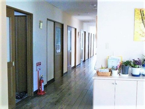 まっすぐな廊下には消火器も設置されている。ダークブラウンの居室ドアが並び、明るい雰囲気。