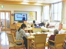 施設内のリビングに集まっている高齢者とスタッフの様子。日中の様子を写したもの