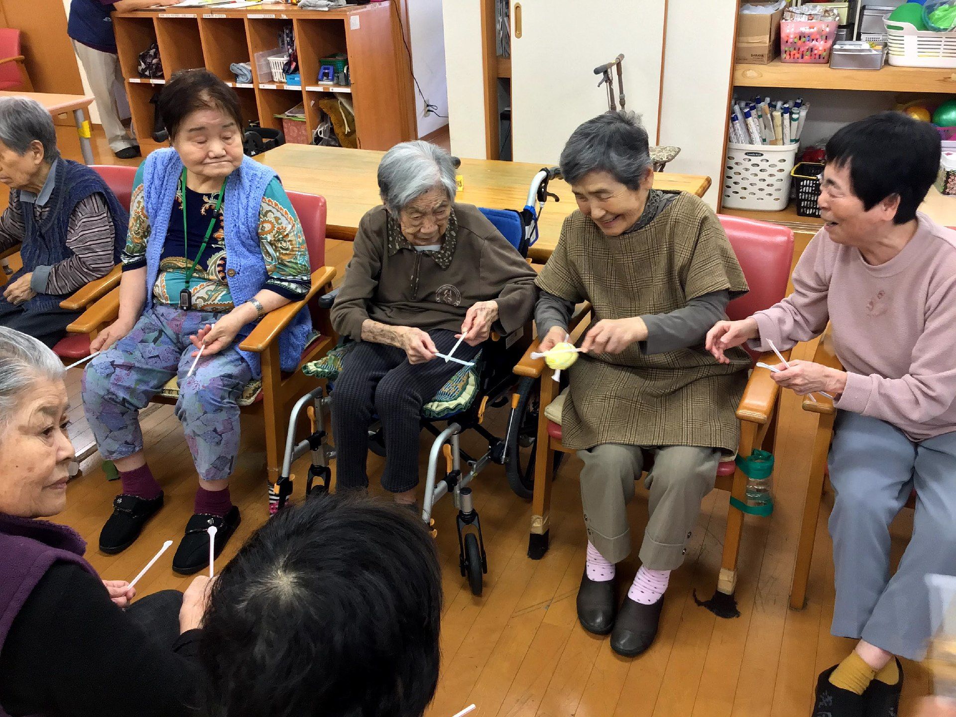 箸を使ってボールのようなものを隣の人に渡すゲームを楽しむ入居者たち。