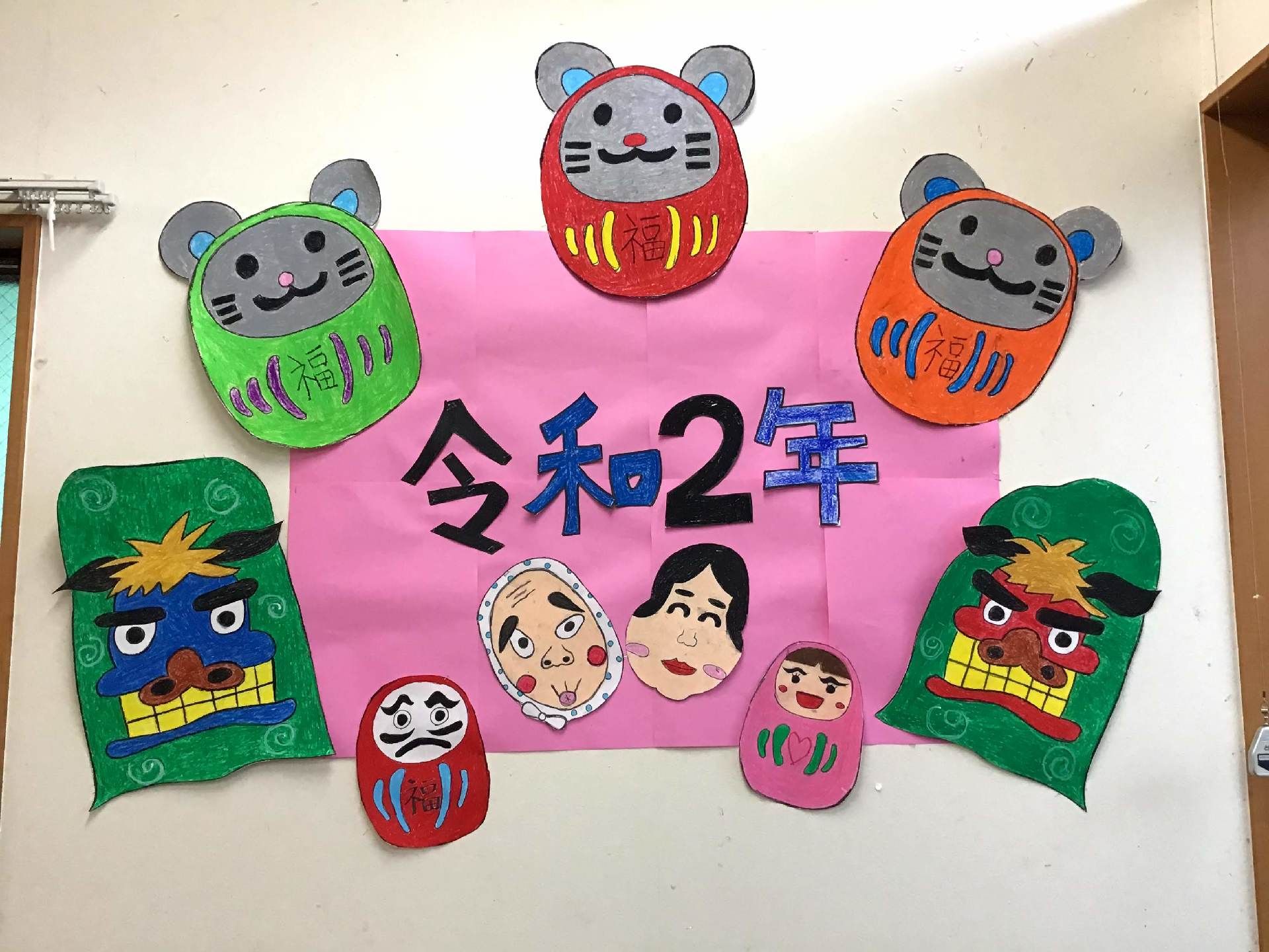 「令和２年」と書かれたピンクの画用紙にはひょっとことおかめのイラストが描かれ、それを囲むようにネズミや獅子舞が飾られている。