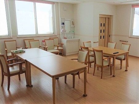 大きな窓があり明るい。ダイニングテーブルが複数置かれ、背もたれの高い椅子がセットされている。