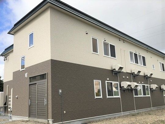 ブラウンと白の2階建ての建物。。窓がたくさんつき、建物の近くには原っぱがあり、自然が多い。