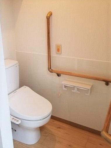 エル字型の手すりが設置されたトイレ。オレンジの呼び出しボタンもトイレットペーパーホルダーのそばについている。