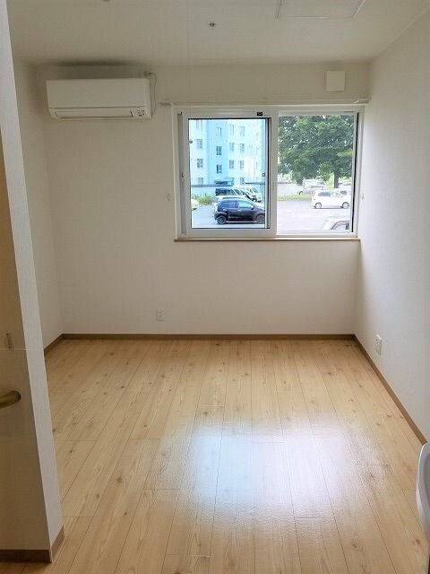 シンプルで家具が置かれていないフローリングの居室。壁にはエアコンが付き、大きな窓にはカーテンが付いていない。