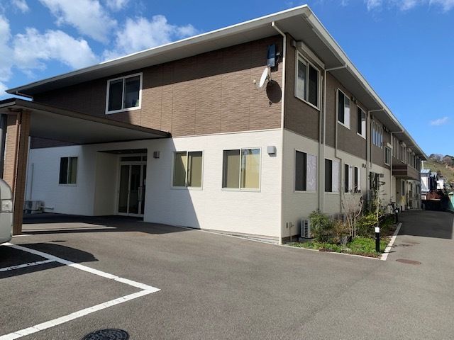 幅の広い2階建ての施設。建物の周囲はアスファルトで舗装されており、自動車が数台駐まっているのが見える。