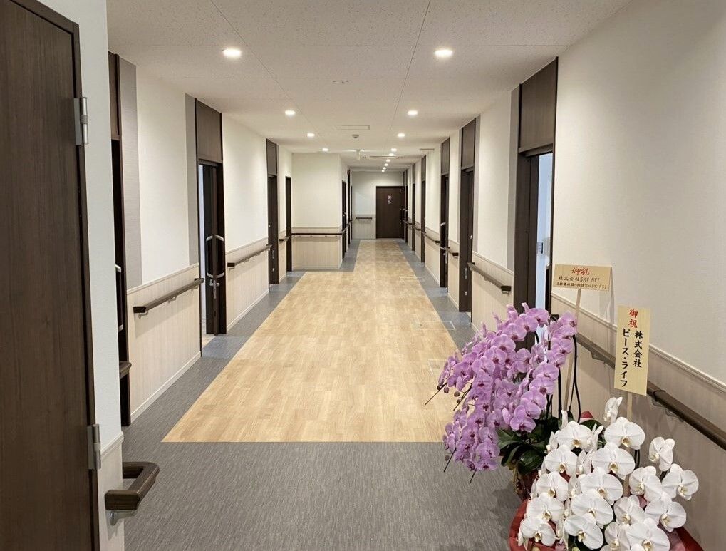 まっすぐな廊下には両側に手すりが付き、ダークブラウンの居室ドアが並び、お祝いの蘭の花も飾られている。