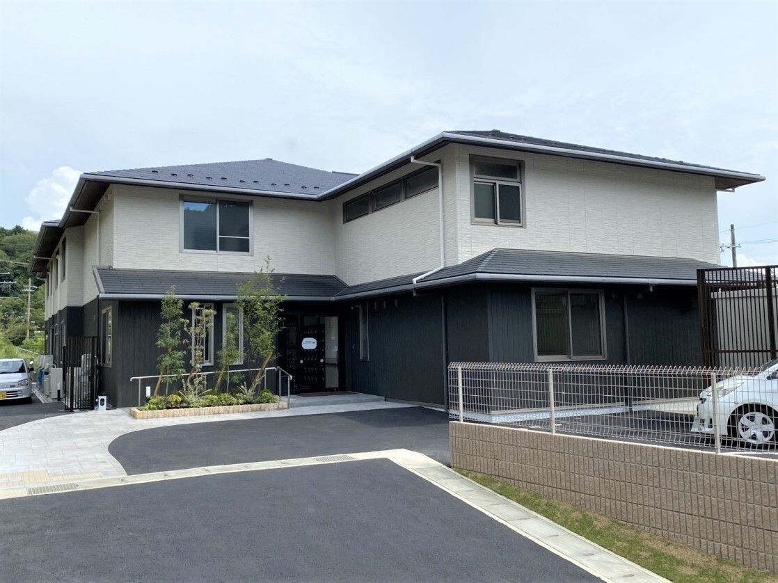 白とダークグレーの2階建ての建物。建物には三角屋根が付き、敷地内には駐車場も完備されている。