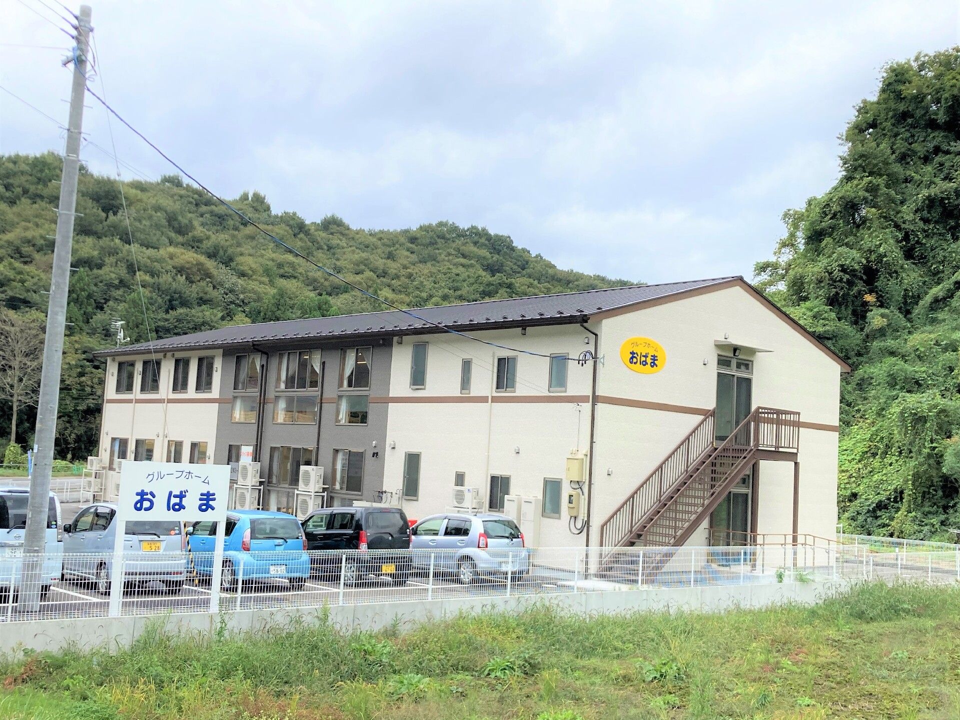 白い介護施設の外観と、車が複数台停まっている駐車場