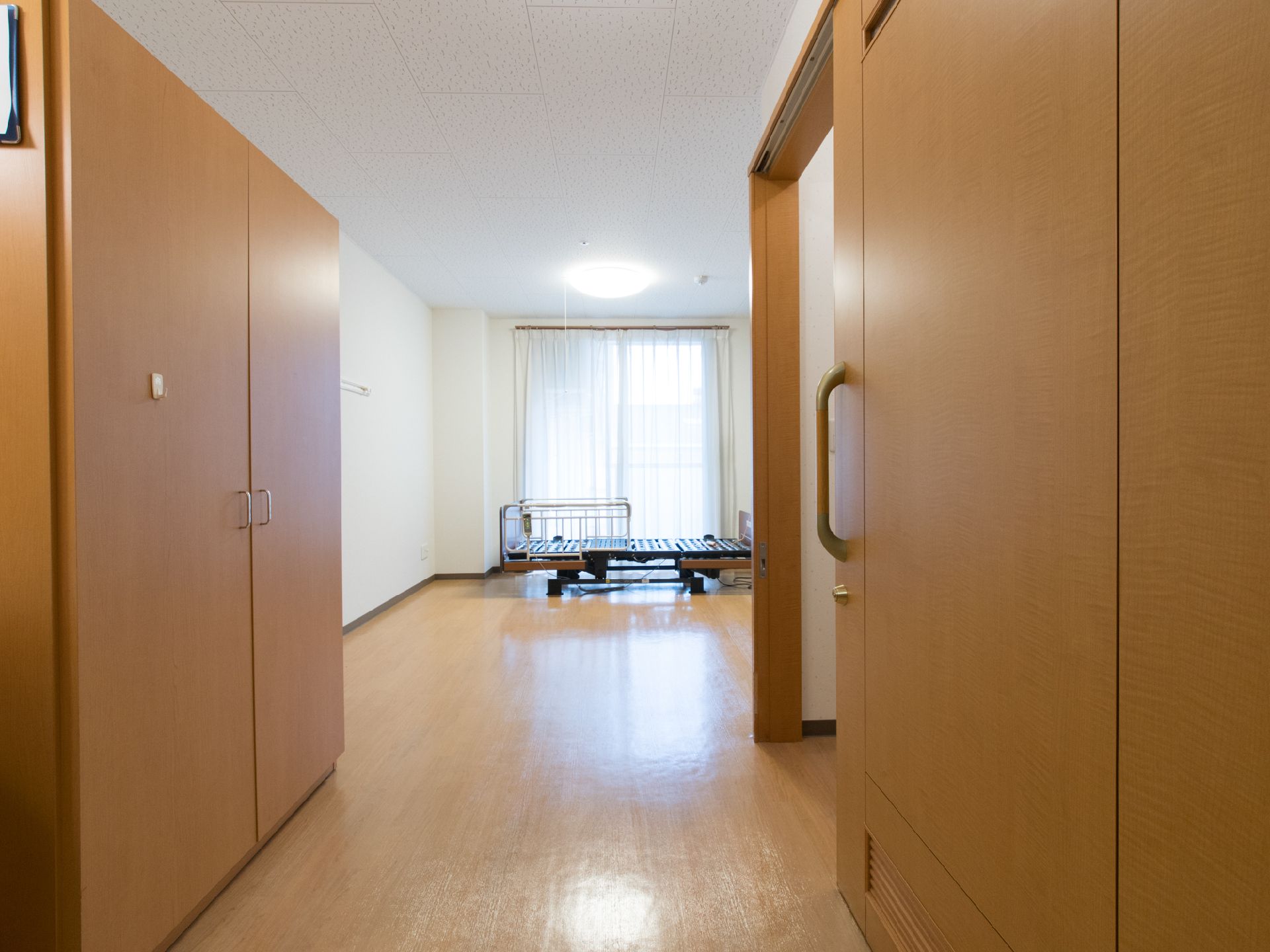 大きな窓のそばに介護用のベッドが設置されている。部屋にはクローゼットも完備。入口付近は広いスペースがあり、車いすの方も安心である。