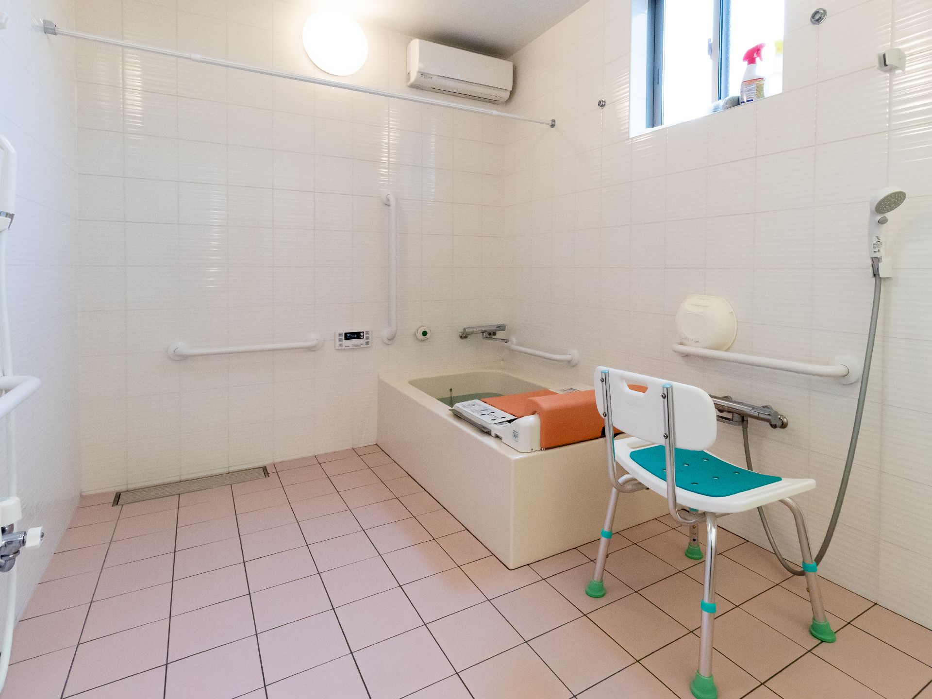 白いポロシャツを着た女性スタッフと車いすの高齢女性が屋外で笑顔で過ごしている。