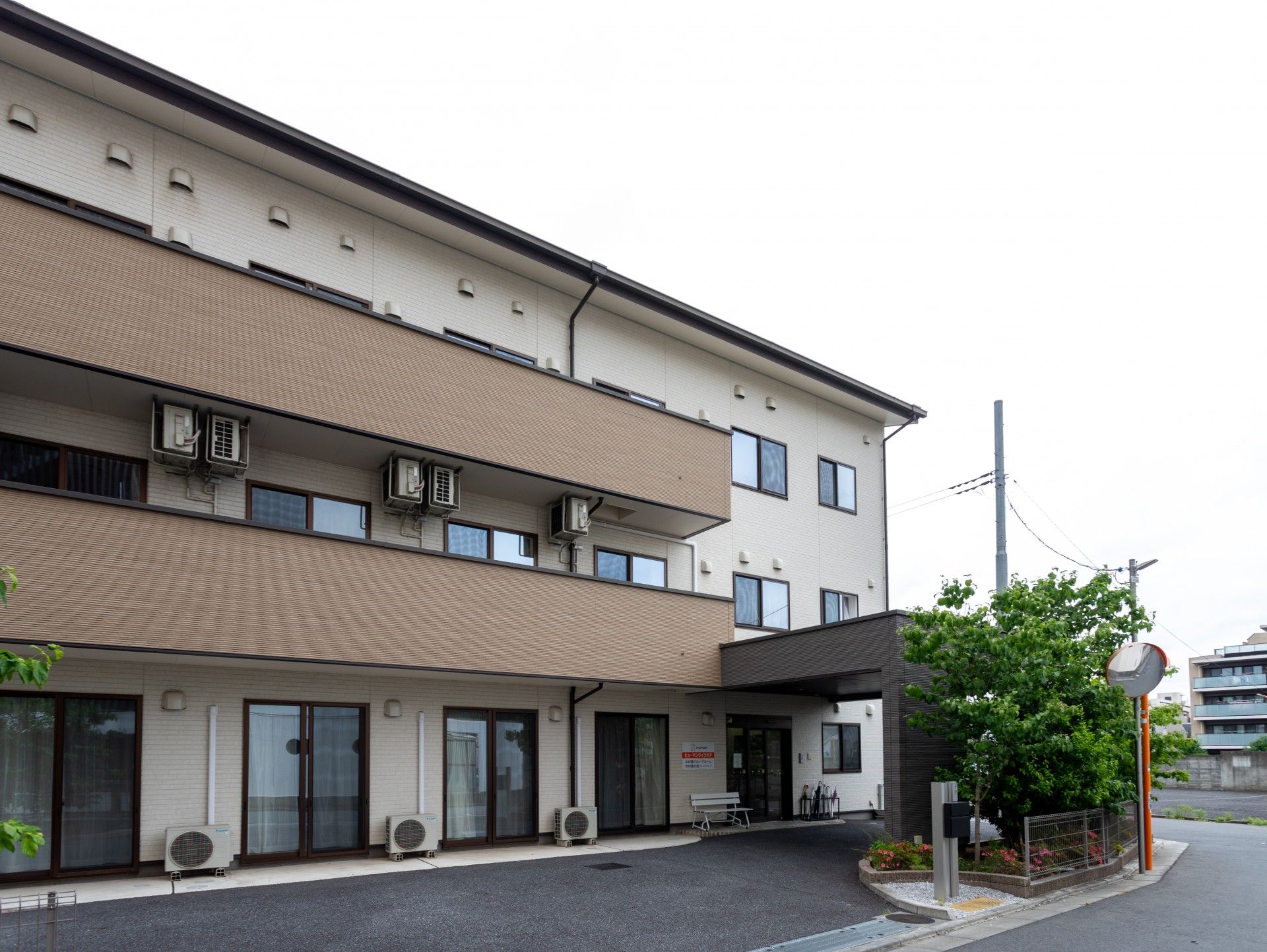 ３階建てで横に長い建物はベランダも設置され、周辺には緑も多く、住宅も点在している。