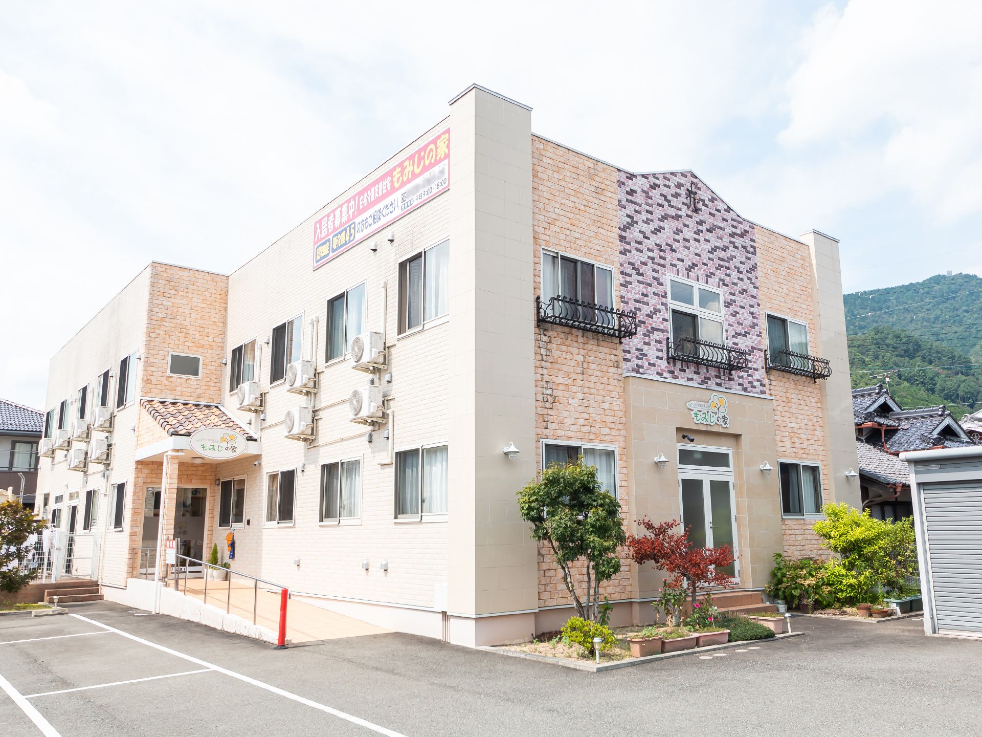 駐車場に隣接した白とベージュの外観で２階建ての建物