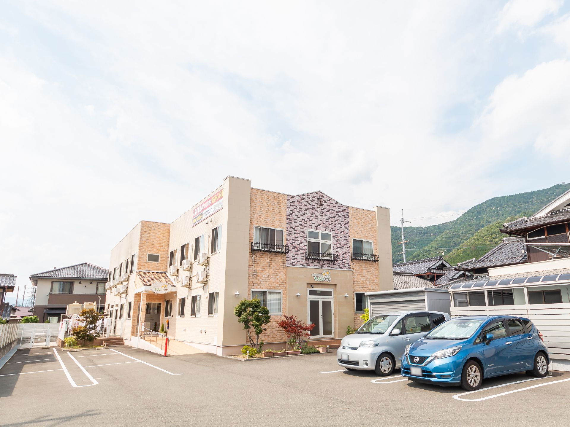 駐車場に隣接した白とベージュの外観で２階建ての建物