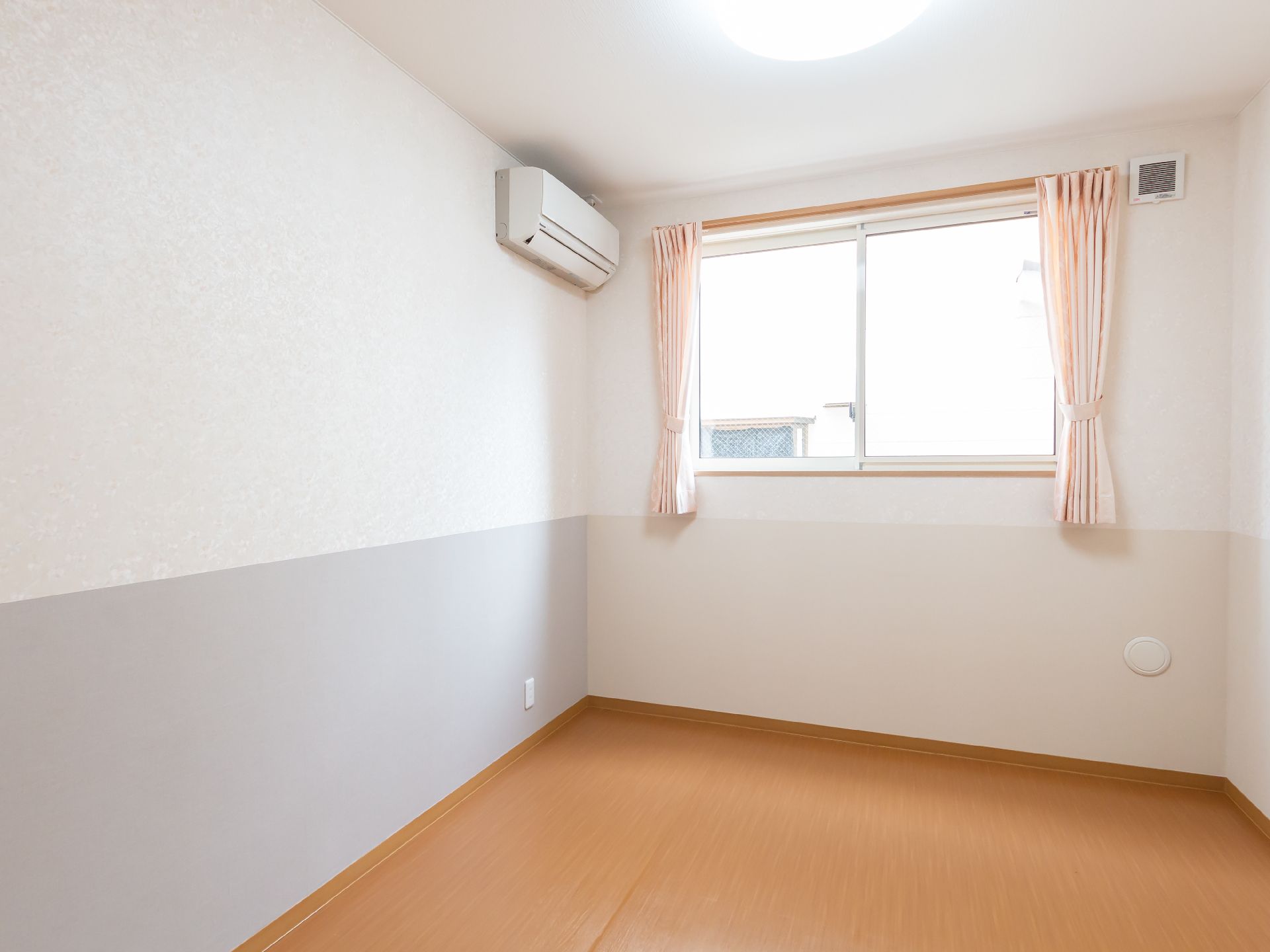 白い壁にエアコンと窓が配置された何も置かれていない部屋
