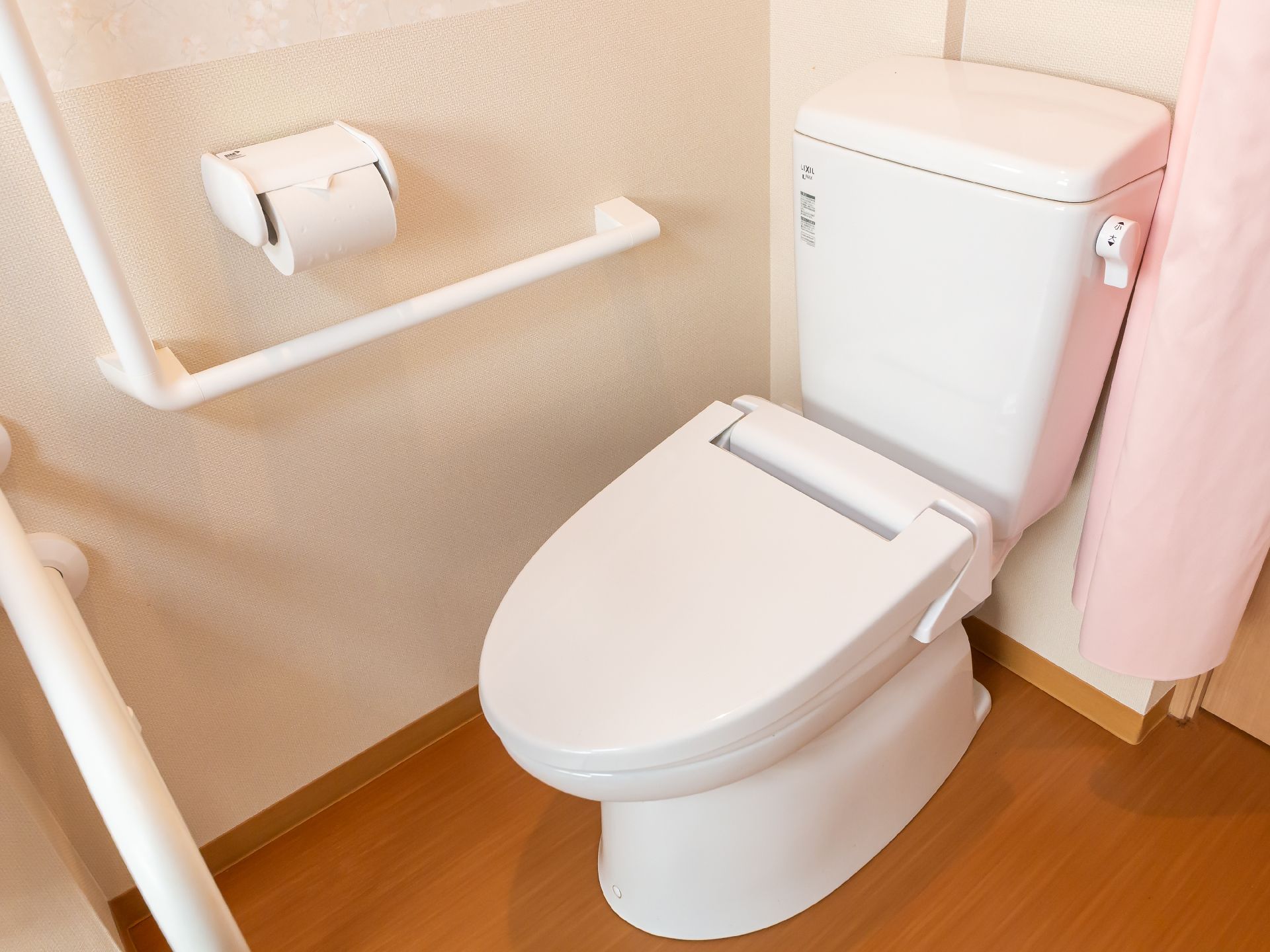 部屋の一角に設けられた白い手すりに囲まれた洋式便器