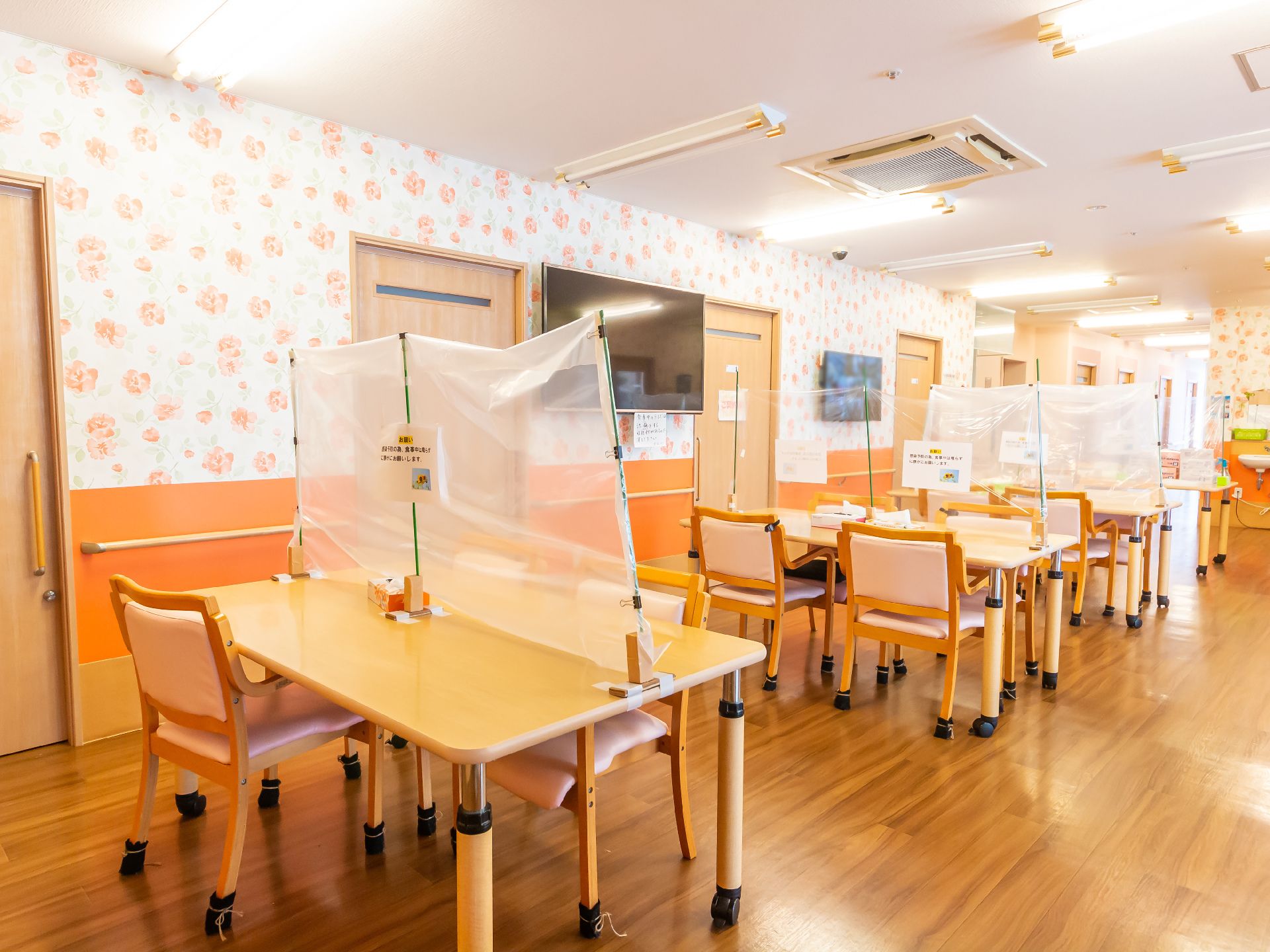 仕切りの設けられた木製の机が並んでいる花柄の壁の広間