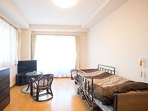 ベッドサイドには緊急通報装置が付き、ベッドには寝具が設置され、テレビの前にはテーブルといすが置かれている。
