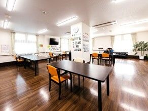 オレンジの椅子がセットされた木製のテーブルが設置された広い共有スペース。大型の壁掛けテレビもある。