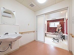 赤い手すりが全域に設置された脱衣所と浴室。脱衣所には車いす対応の洗面所があり、浴室にはリフトやベンチがある。