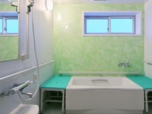 ライトグリーンと白の壁には手すりがたくさんついている。一人用の浴槽が設置され、両サイドにグリーンのベンチがある。