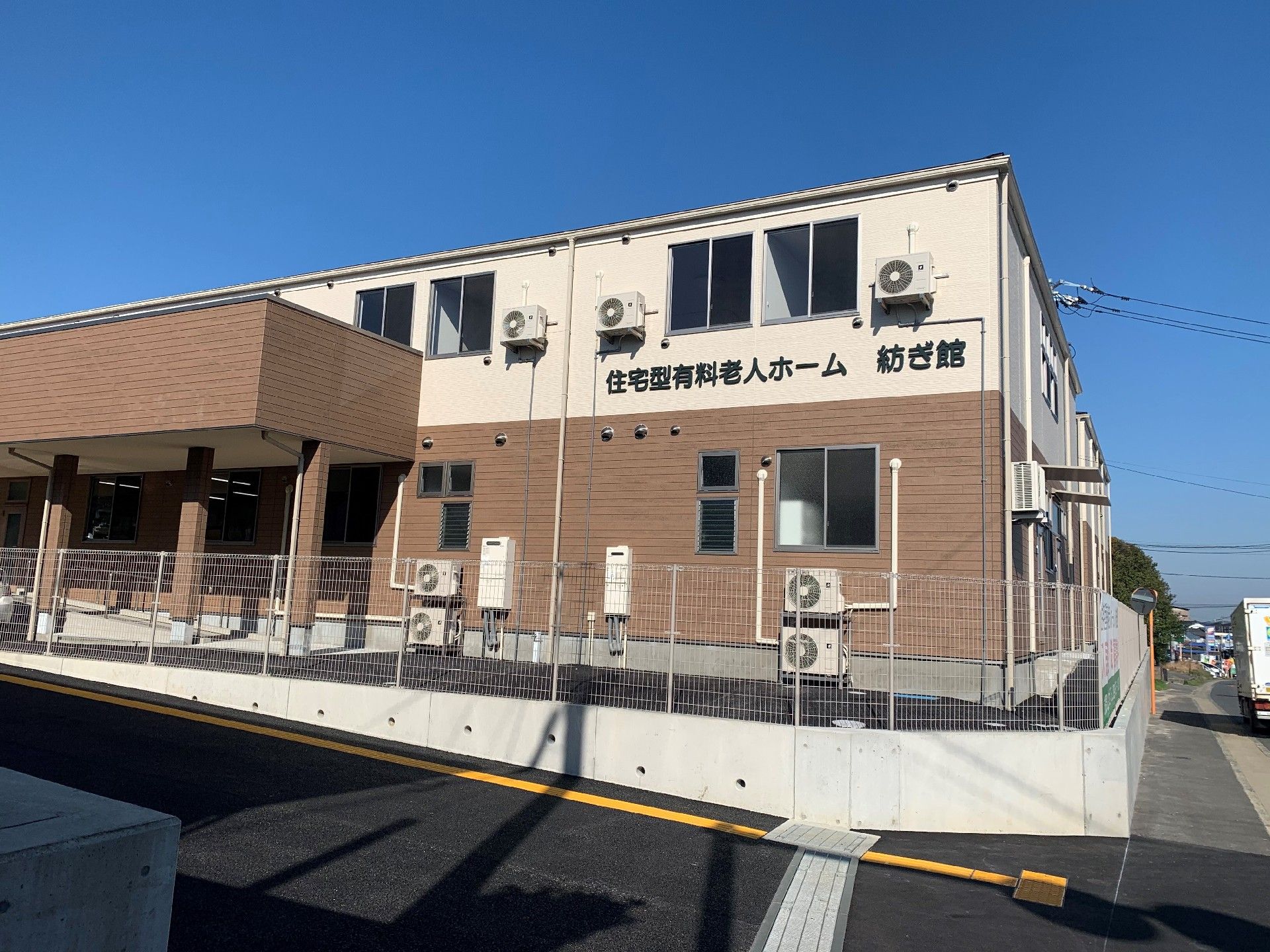 2階建てのブラウンと白の建物は横に長く窓がたくさんあり、玄関にはスロープや屋根もある。