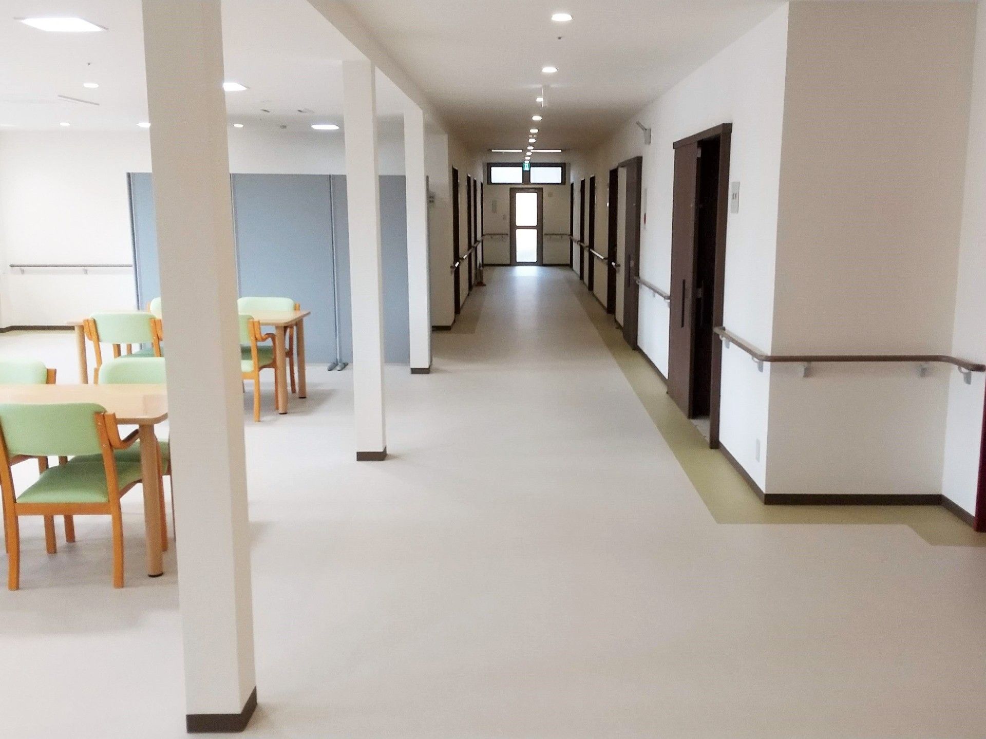 まっすぐな廊下には両側に手すりが付き、ダークブラウンの居室ドアが並び、左側には共有スペースもある。