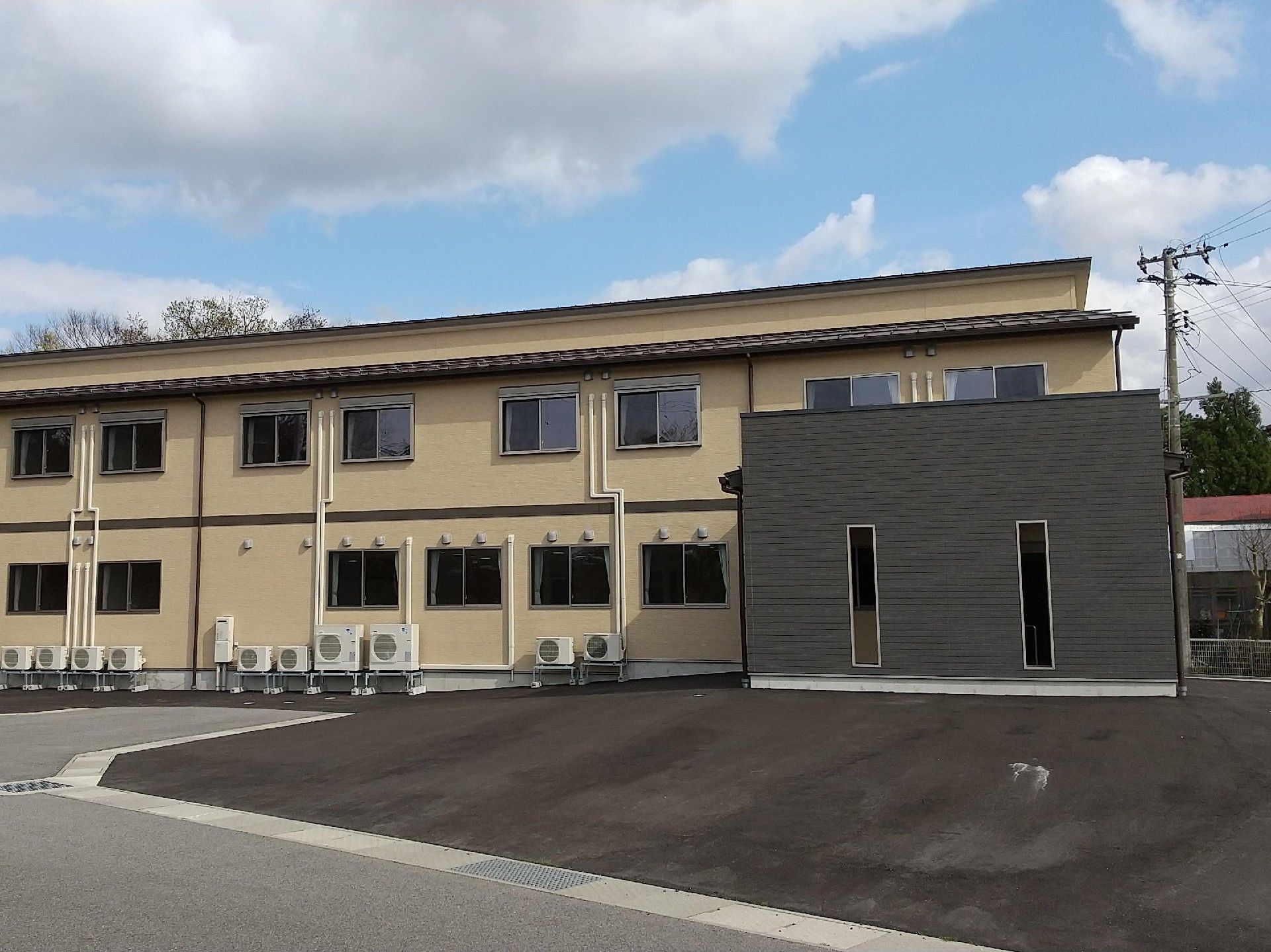車寄せが付いた2階建ての建物。広い駐車場が付き、ホーム周辺には緑もある。