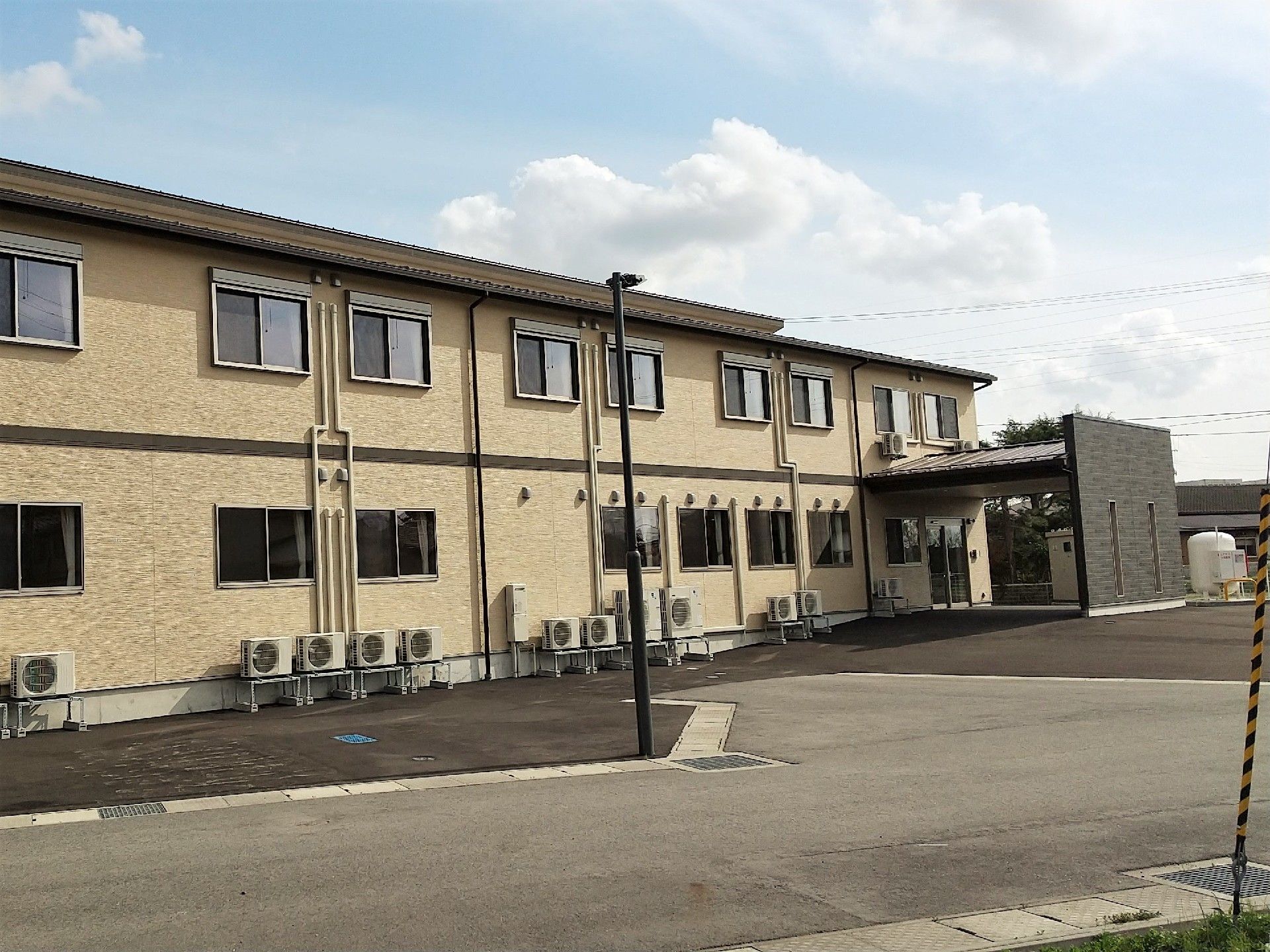 ２階建ての建物。ベージュを基調とし窓がたくさんついている。玄関は車寄せ付き。