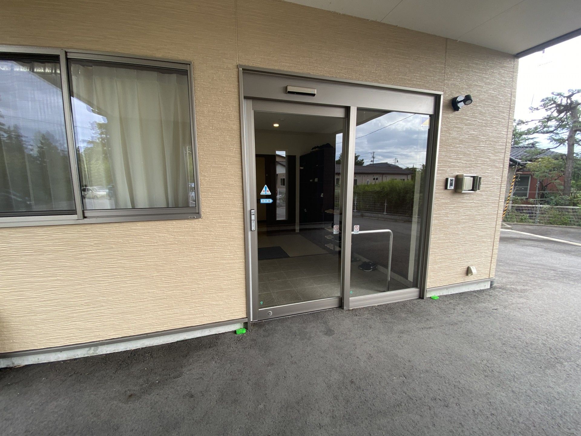 車寄せが付いた2階建ての建物はベージュ系。広い駐車場が付き、日当たりもよい。