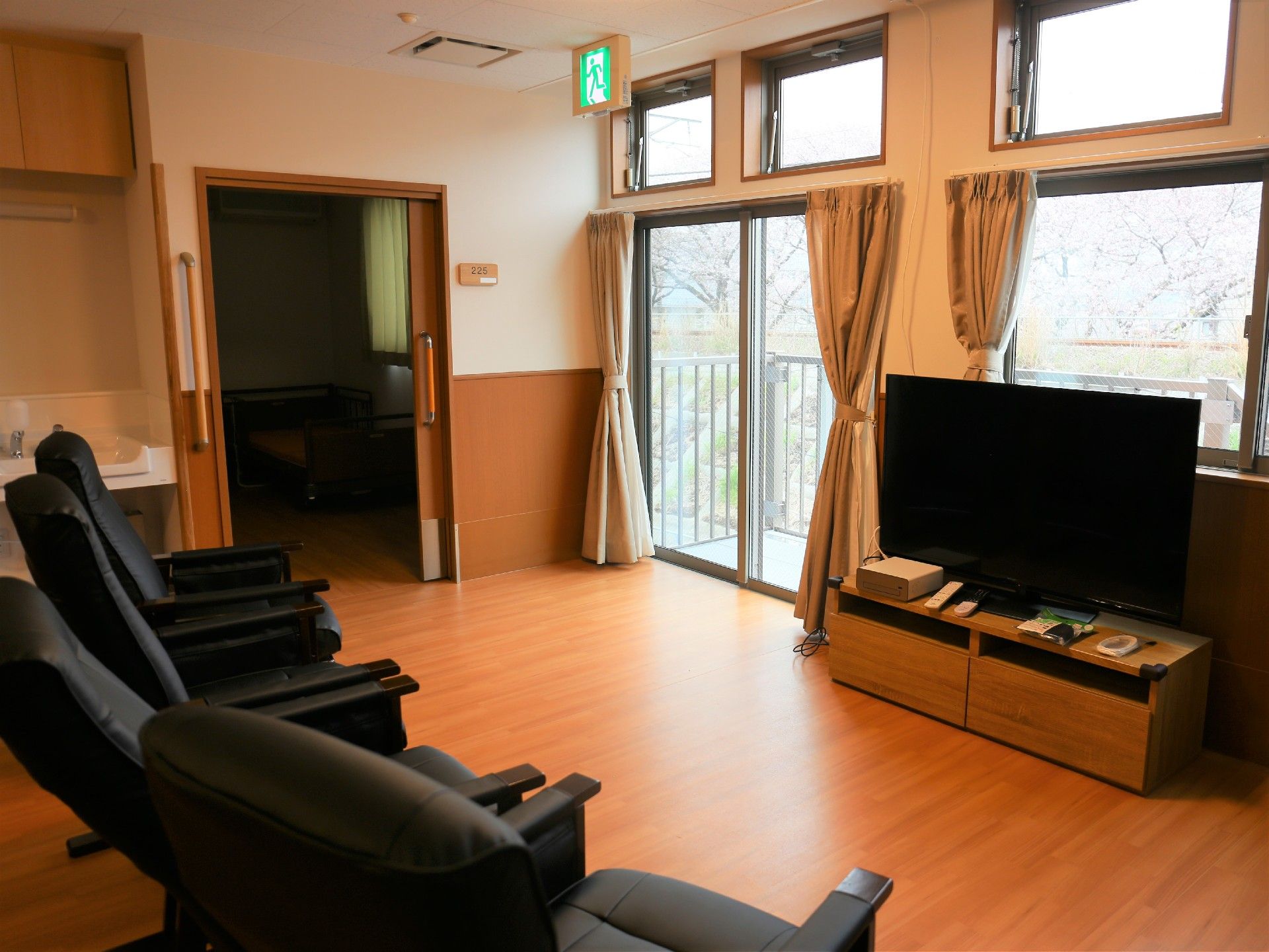 大きな窓のそばにテレビが設置され、テーブルに淡いピンクのシートの椅子が配置された共有スペースである。