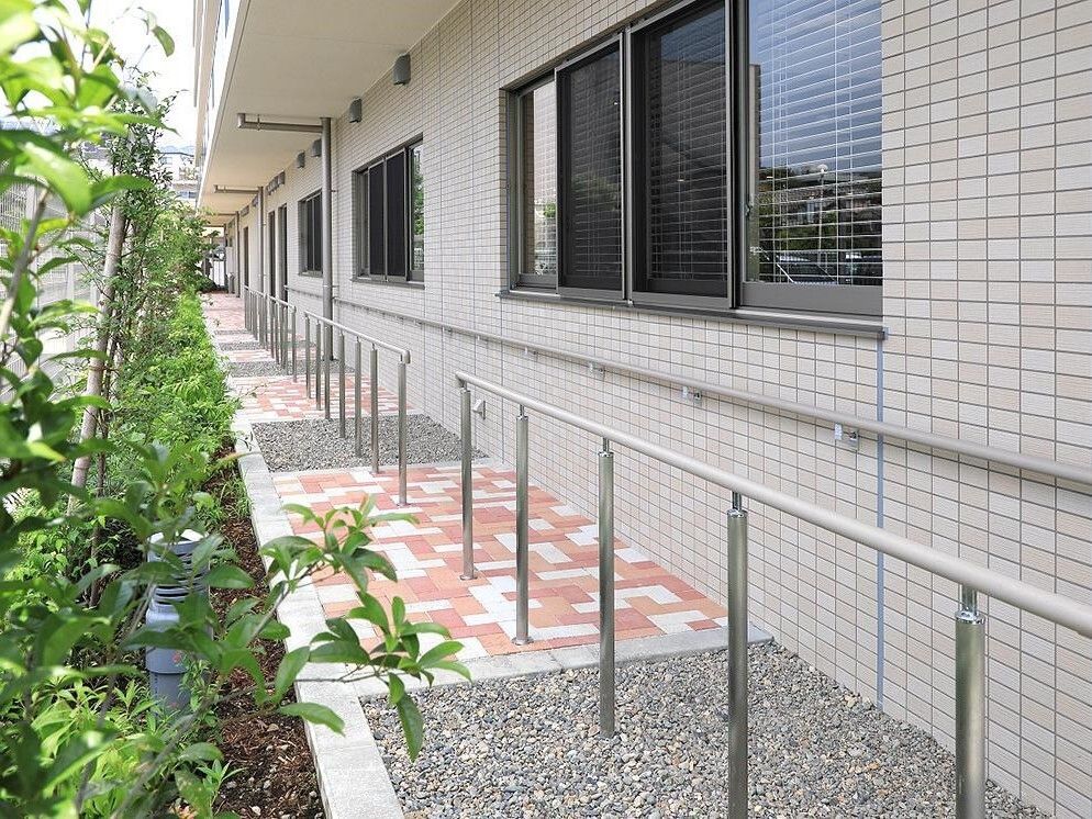 1階の軒下に設置された手すりと、建物の周辺を囲む緑