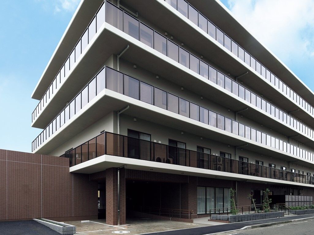 ブラウン系の5階建ての建物。建物前には道路があり、各フロアにベランダがある。