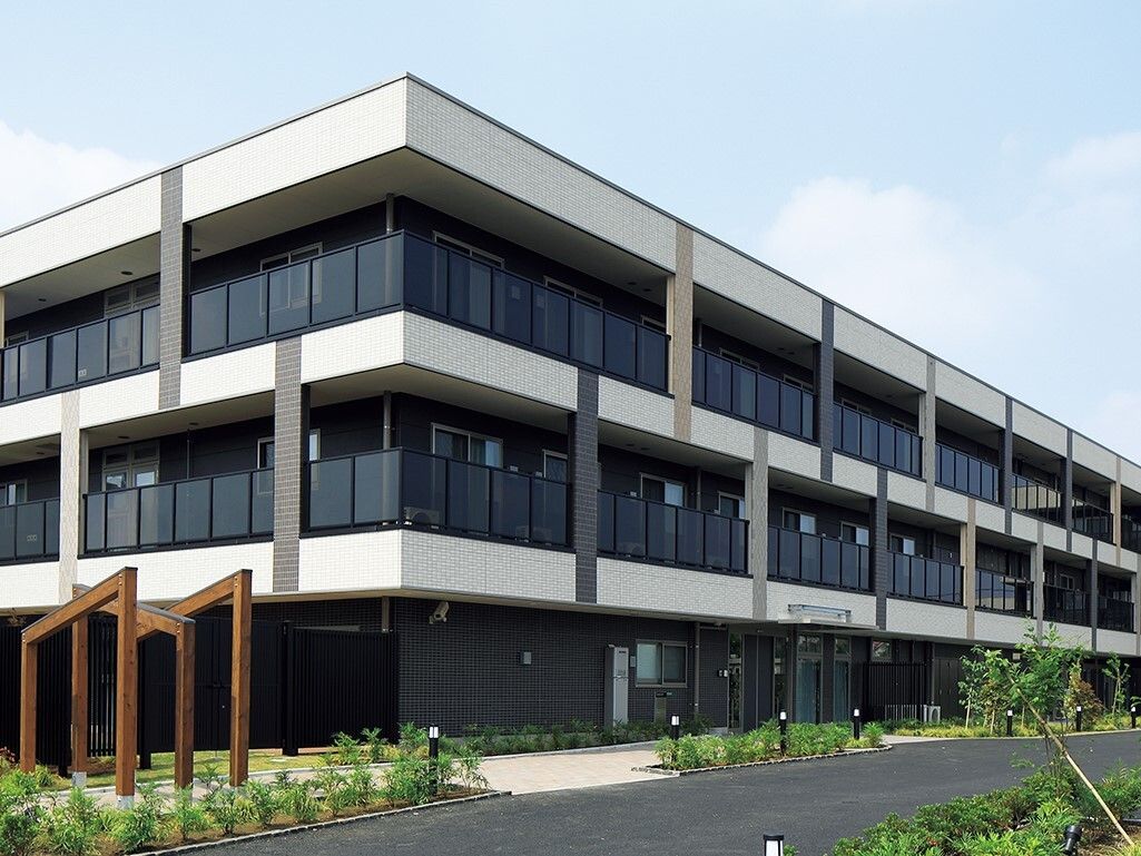 ３階建てで横に長い建物。周辺には緑も多く、建物は白とブラウンで落ち着いた雰囲気。