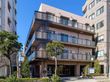 ベランダ付きの４階建ての建物。明るめの色をメインとしているため圧迫感がなく、建物の前には緑もある。
