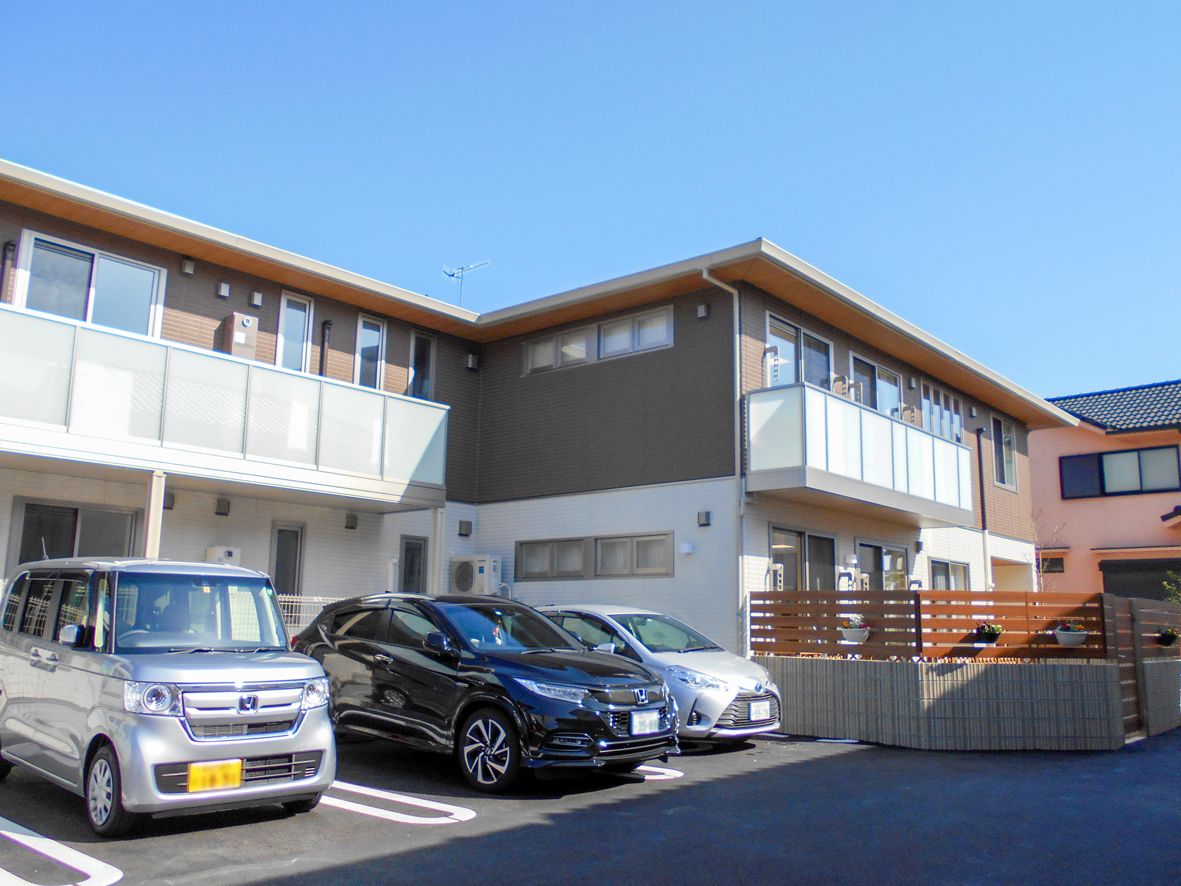日当たりのいい場所に建っている２階建ての建物は白とブラウンの外壁で、ベランダが付いている。