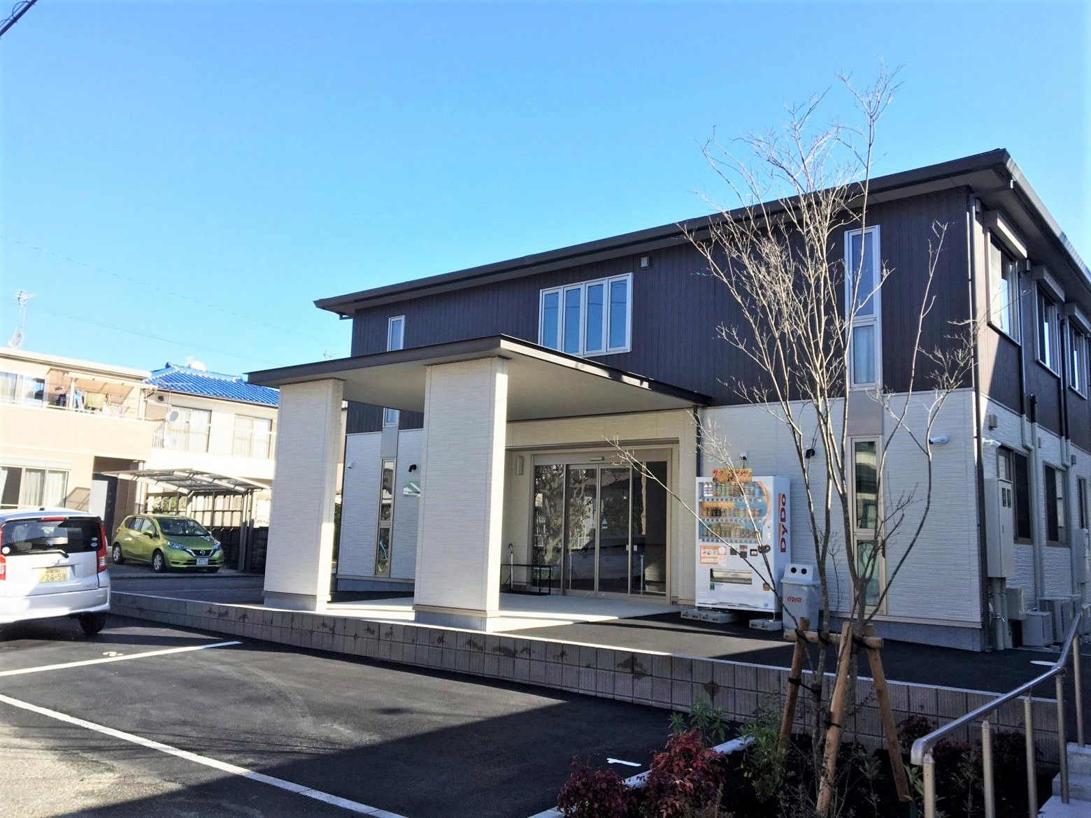２階建ての建物。１階部分は白、２階部分はダークグレーで駐車場がある。