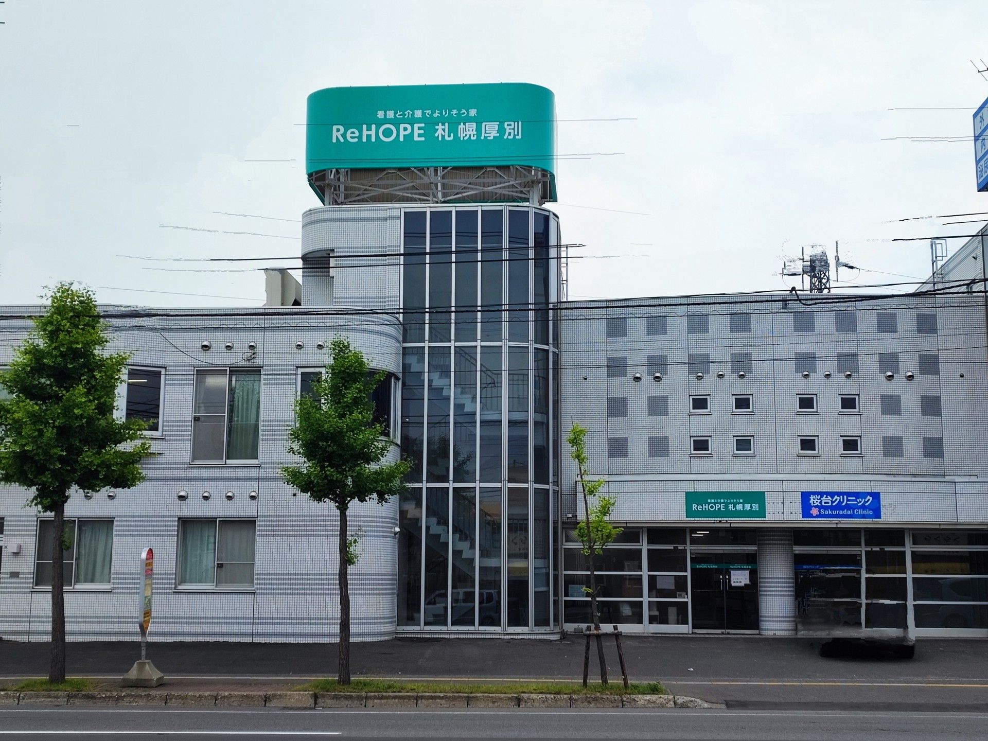 エメラルドとブルーの看板が設置された白っぽい建物。周辺に住宅はなく、道路に面している。