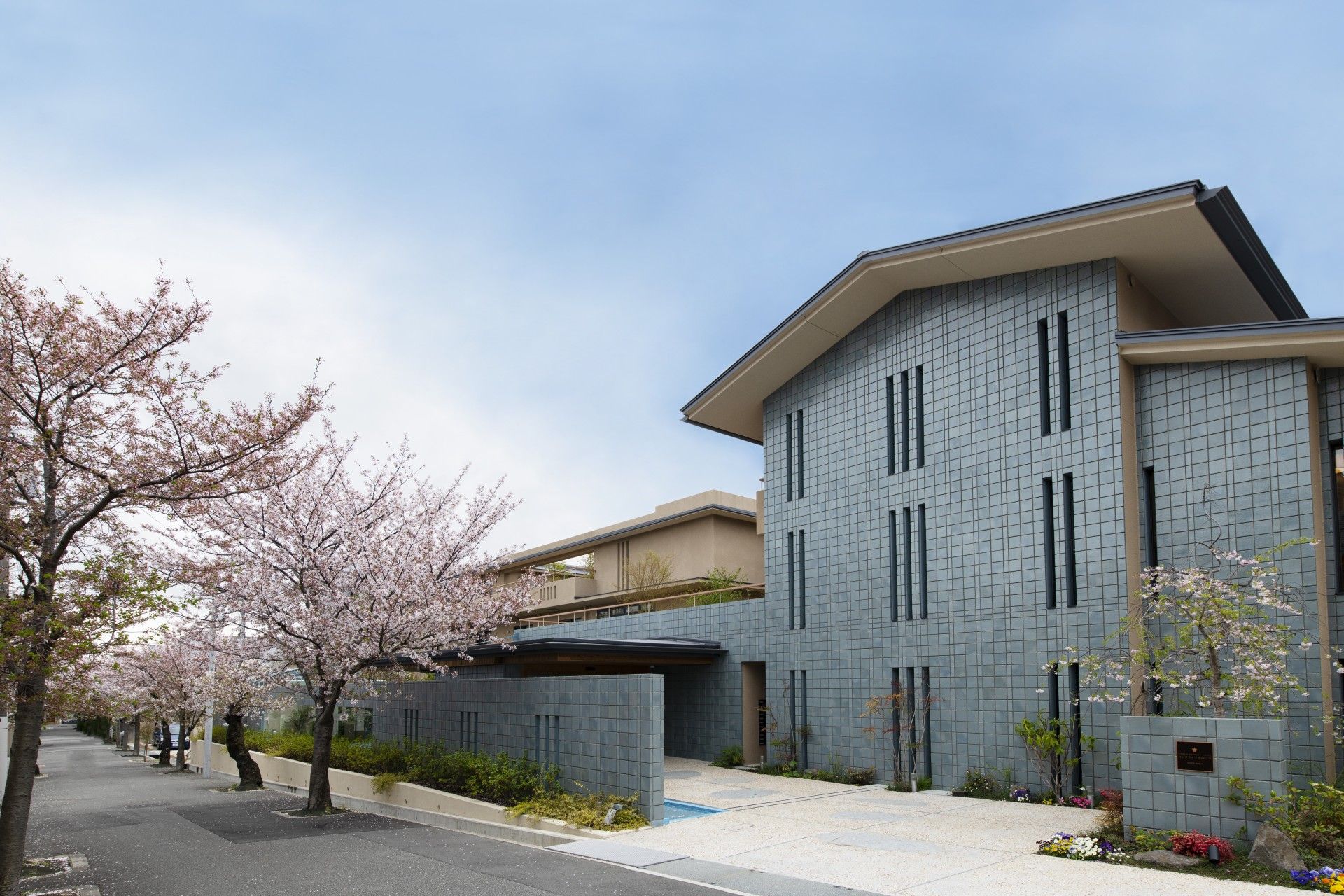 桜の木に囲まれた敷地内には3階建ての建物が建っていて、駐車スペースには車が止まっている。