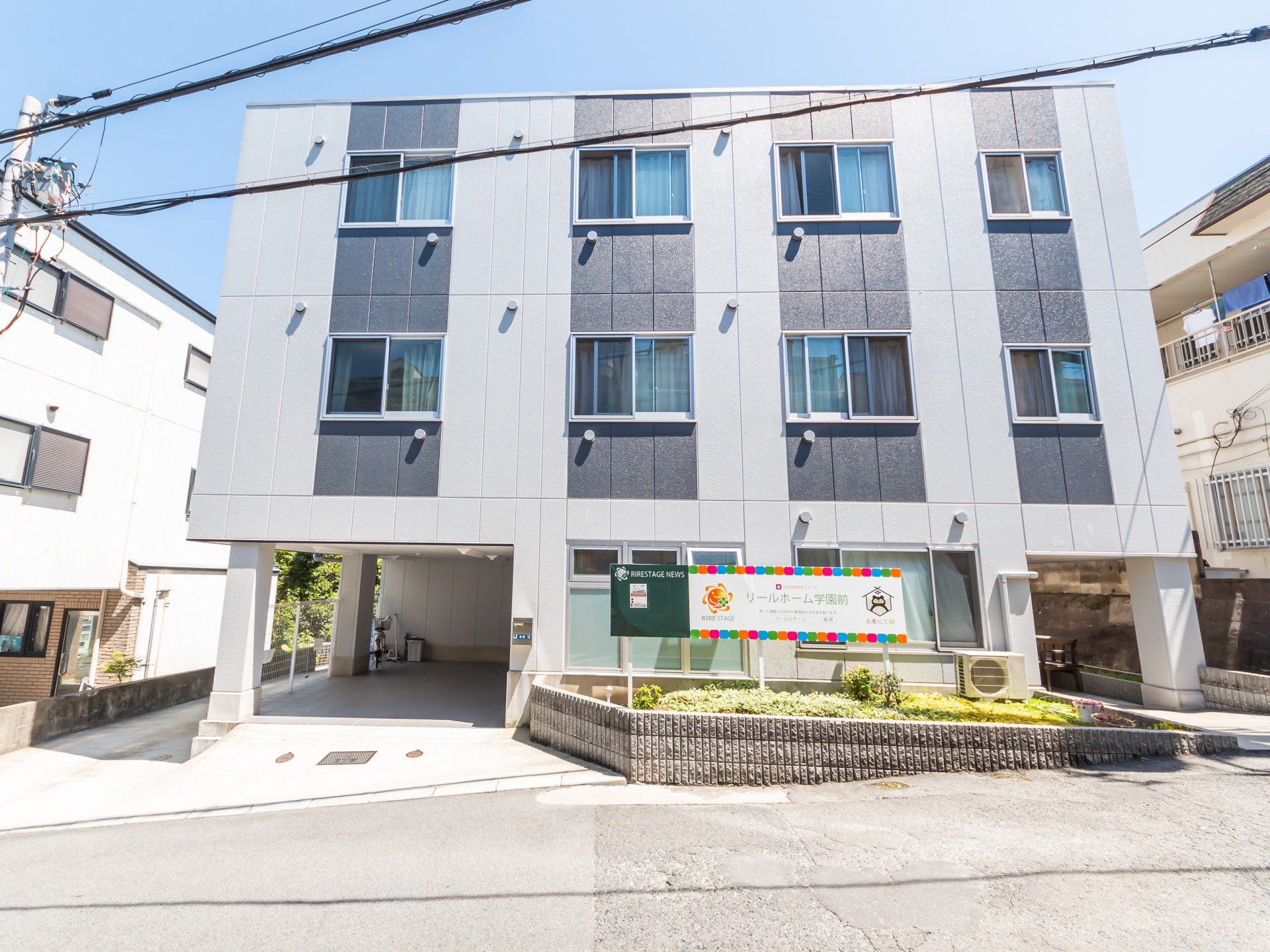 グレーの4階建ての建物には窓がたくさんつき、外壁には濃いグレーのラインが建てに4本描かれている。