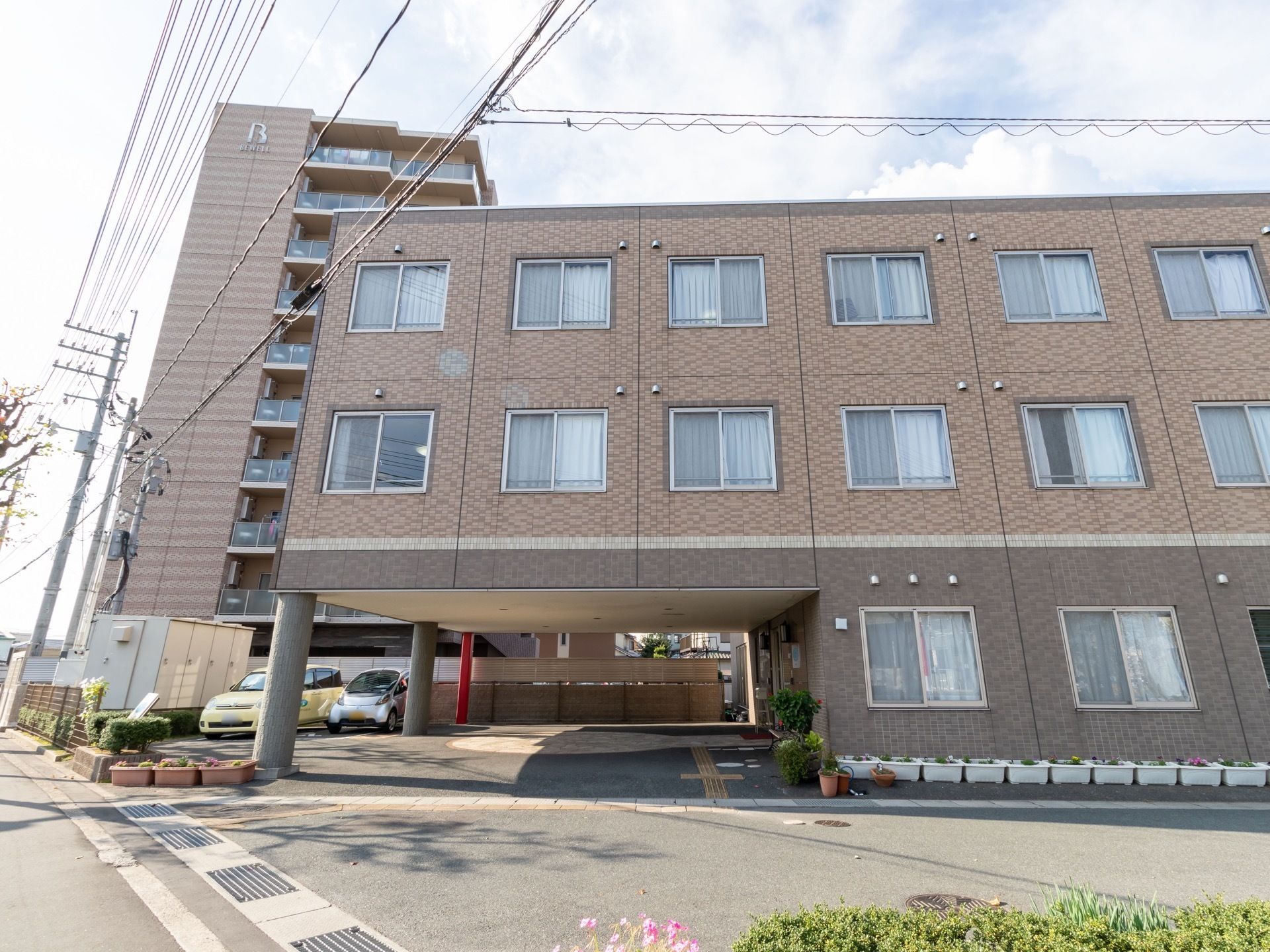 １階の一部を車寄せとして利用している。建物の周囲にはプランターが置かれ、色とりどりの花が飾られている。