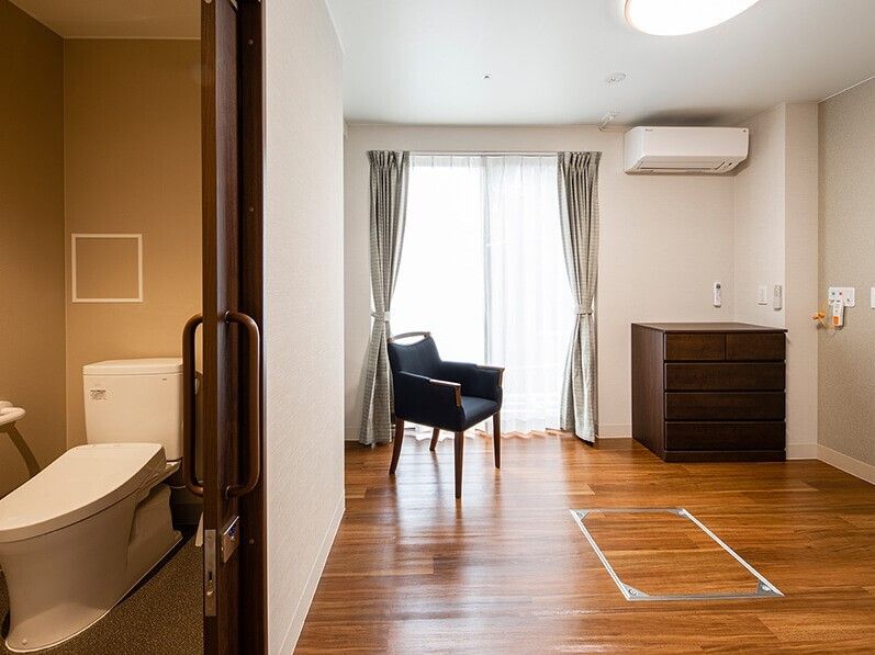 広々としたフローリングの部屋にはトイレが付き、エアコンやタンス、椅子も置かれ、緊急通報装置もある。