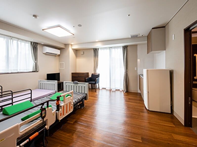 大きな窓が二つ付いた広いフローリングの部屋には介護用ベッドが二つ置かれ、キッチンやテレビ、エアコンもある。