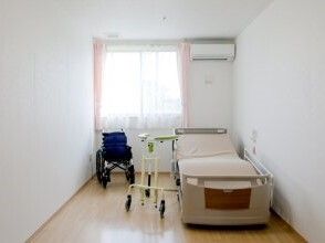 大きな窓があり明るい雰囲気。居室には、ベッドだけでなくエアコンもつき、車いすや歩行器が置かれている。
