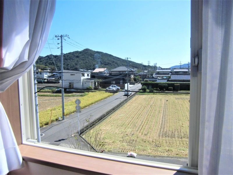 稲刈りをしたばかりの田が広がっていて、その奥には民家がある。居室の窓から見た様子。