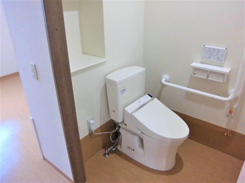 オレンジの呼び出しボタンが付いたトイレにはエル字型の手すりもあり、温水洗浄便座が付いている。